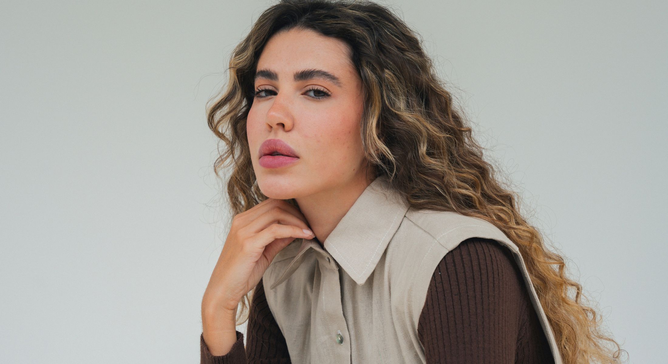 Woman with curly hair posing thoughtfully indoors.