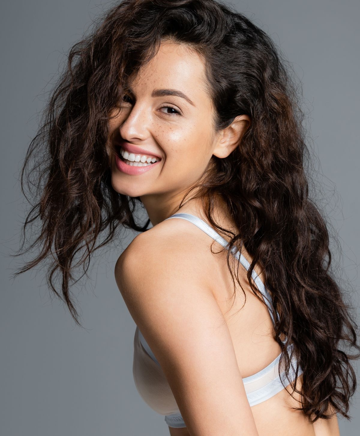 Woman with curly hair smiling over shoulder.